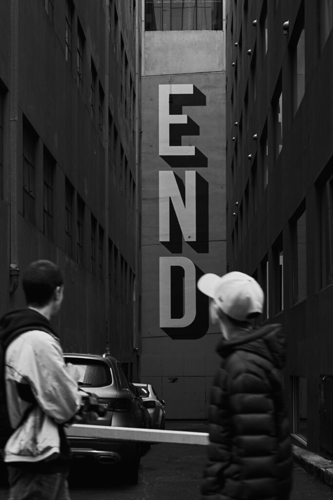 A black and white photo of people past  a street with a sign that says end. Taken By Aidan McCorry | Copyright Aidan McCorry Chromatic Times